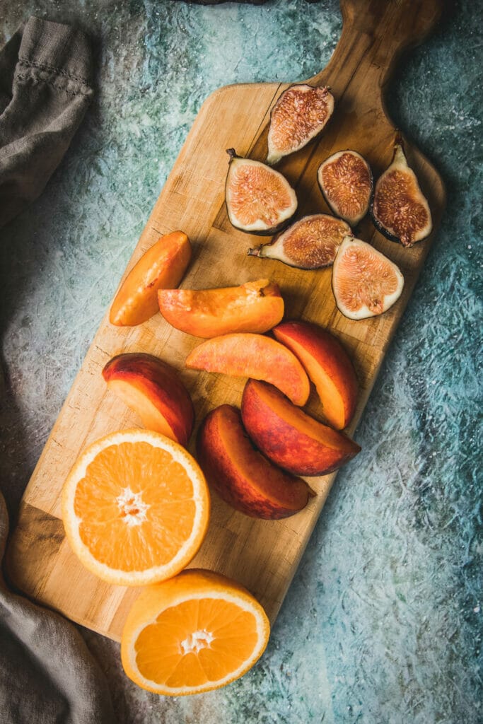 cutting board with chopped oranges, peaches, and figs shot from overhead