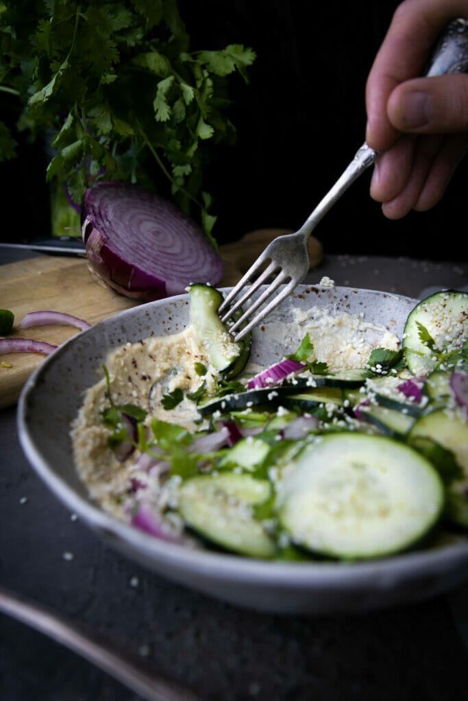 fork scooping cucumber salad into tahini sauce