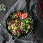 overhead view of green bowl of strawberry quinoa salad with a silver spoon on a grey table
