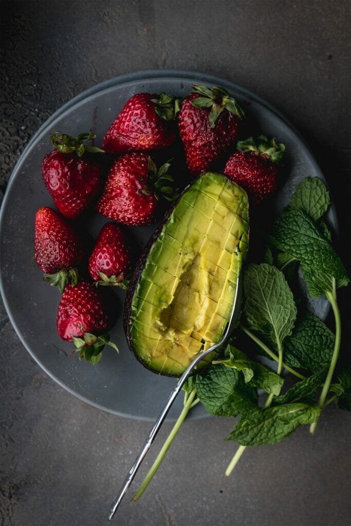 grey plate with one avocado half and 8 full strawberries
