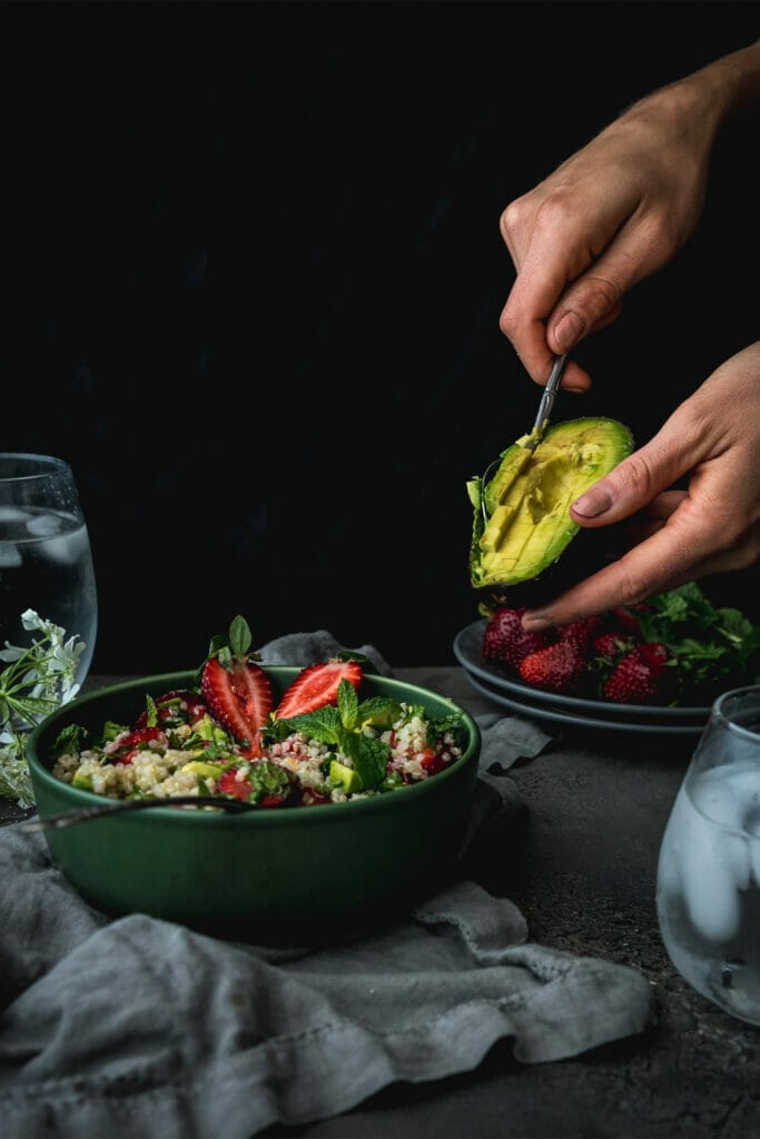hand scooping avocado into a bowl of strawberry quinoa salad