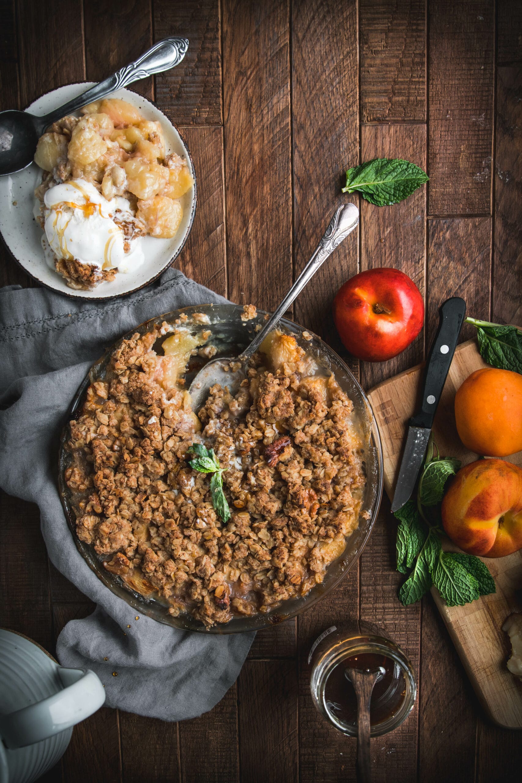 spoon digging into a brown butter bourbon peach crumble on a wooden table