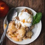 serving of brown butter peach crumble on a white plate with ice cream and mint