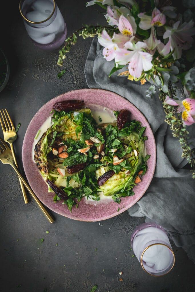 overhead shot of green grilled cabbage on a plate next to a vase of flowers
