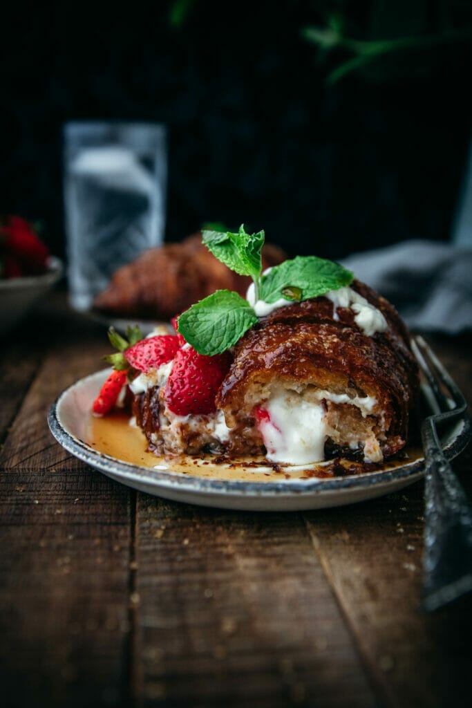 cinnamon crunch croissant french toast on a white plate with mint and sliced strawberries