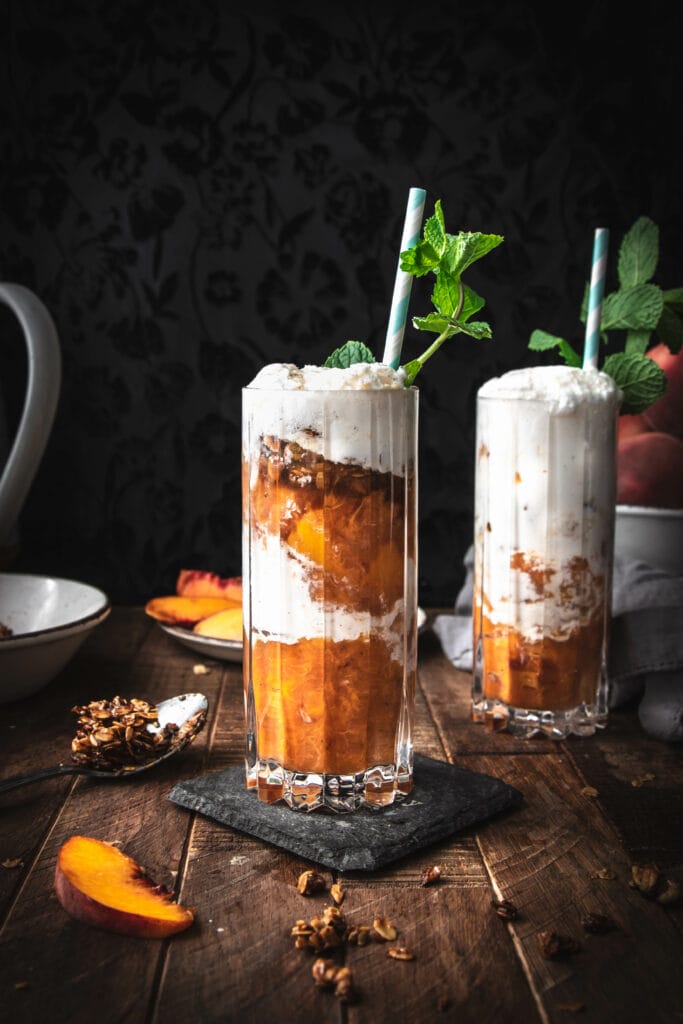 two glasses of peach crumble ice cream floats topped with mint on a wooden table