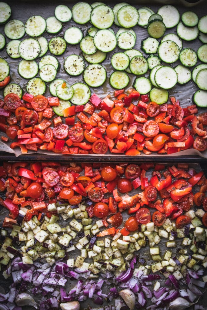 overhead shot of two baking sheets with roasted ratatouille ingredients of zucchini, cherry tomatoes, red peppers, and eggplant