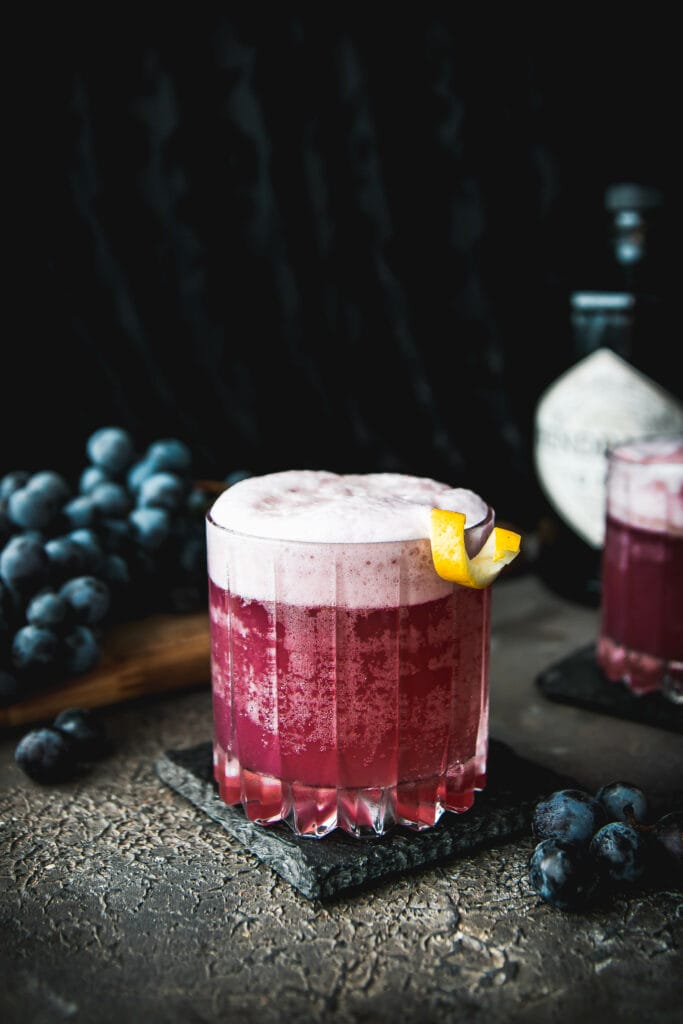 one glass of concord grape gin fizz cocktail with a lemon twist