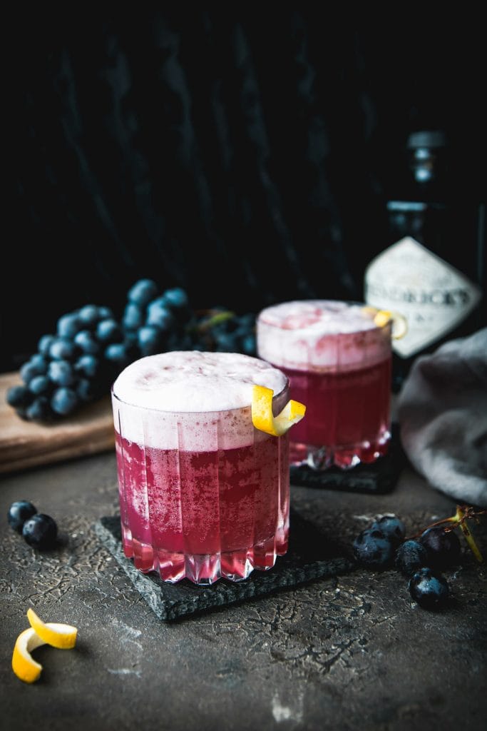 two glasses of concord grape gin fizz cocktails with a lemon twist