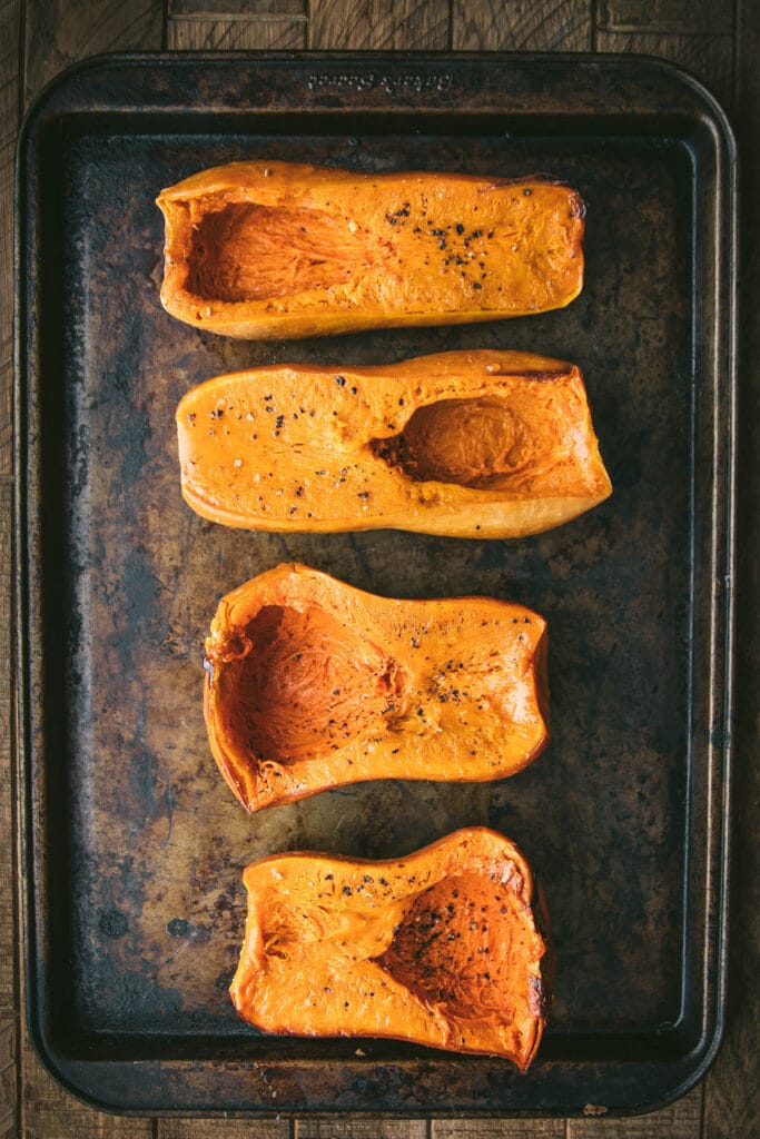 four halves of roasted honeynut squash on a baking sheet