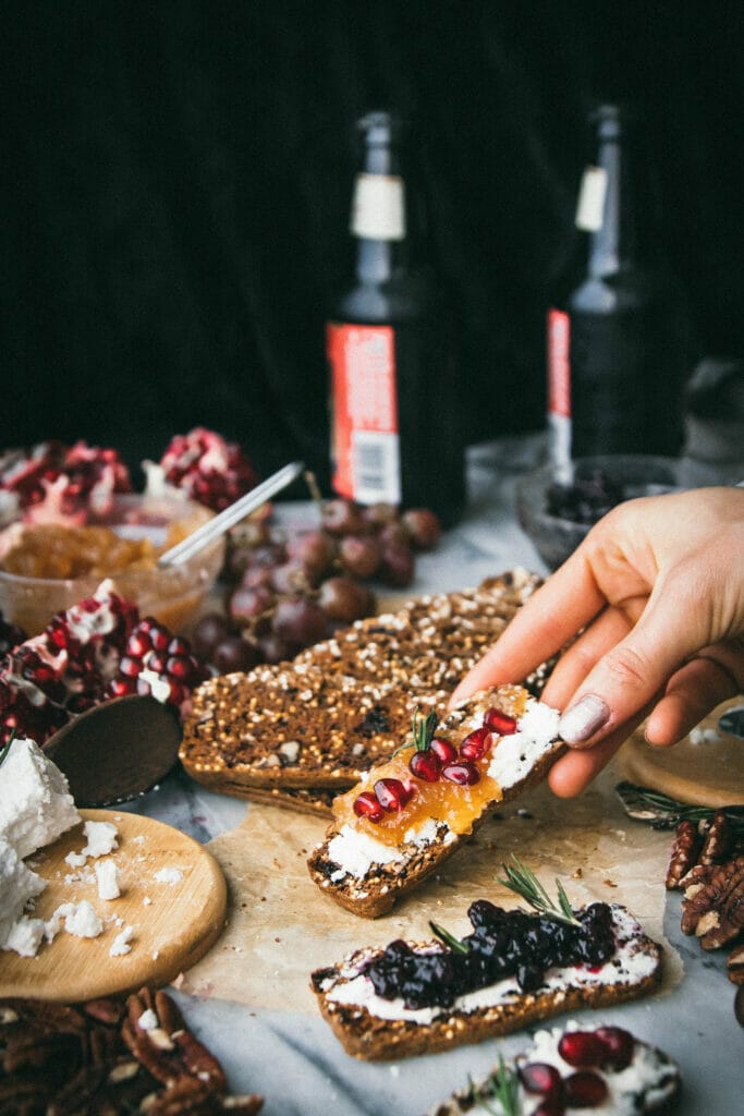 hand reaching down to grab a gourmet cracker with goat cheese and pomegranate on top