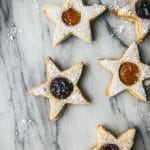 five vegan linzer cookies with jam on a marble tray