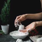 hands rolling a walnut snowball in powdered sugar