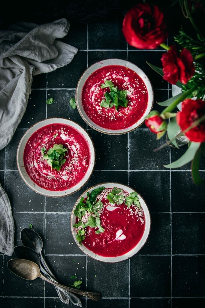 overhead shot of three bowls of beet carrot ginger soup on a tile table