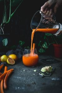 glass pitcher of carrot turmeric ginger juice being poured into a glass