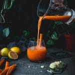 glass pitcher of carrot turmeric ginger juice being poured into a glass
