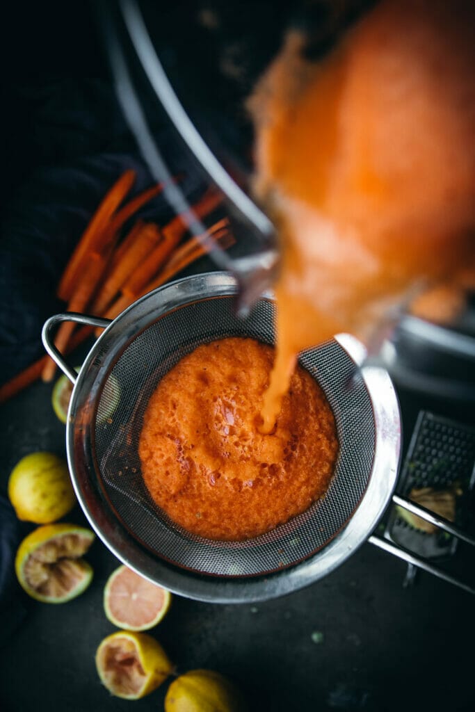 overhead shot of carrot turmeric ginger juice being poured into a strainer