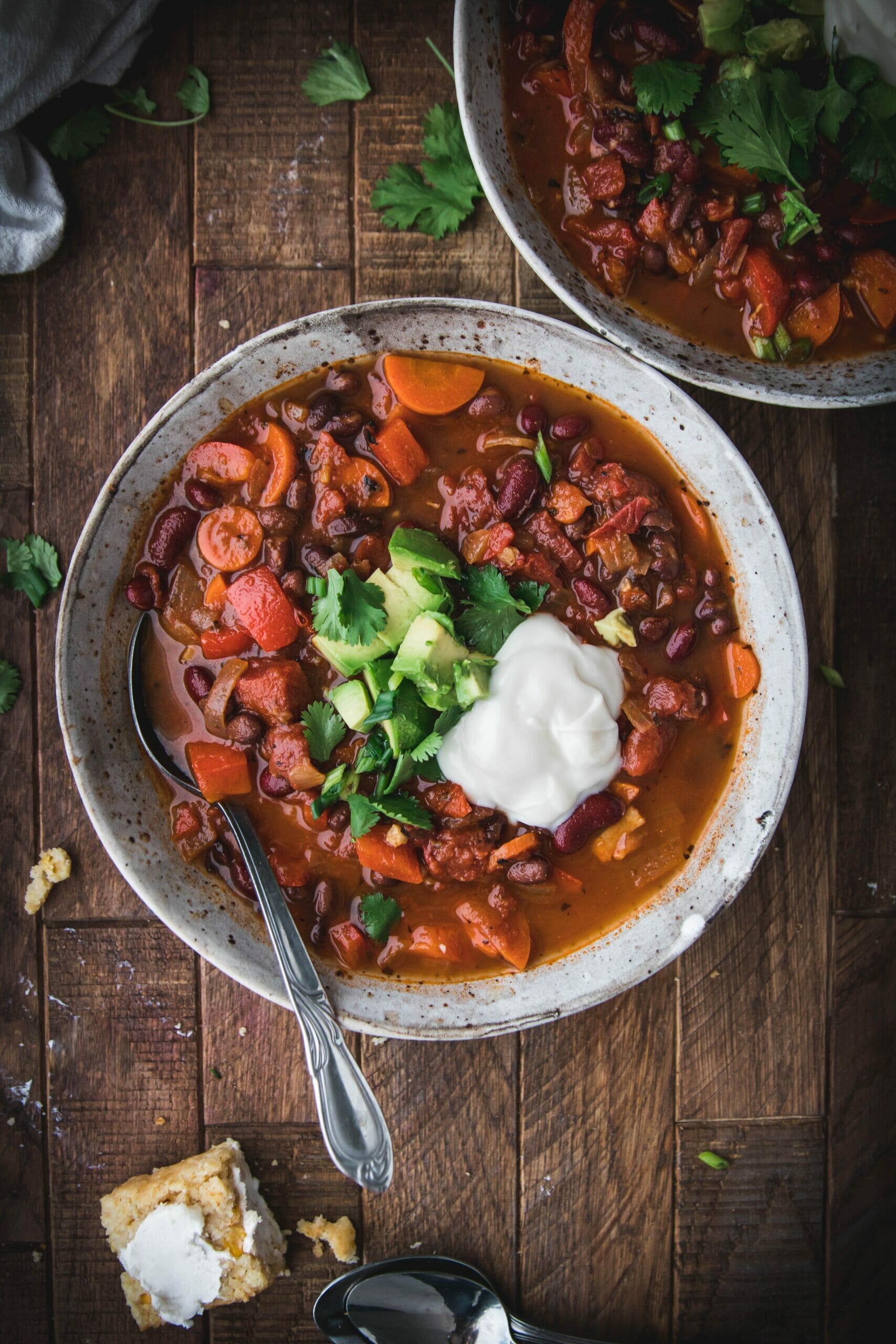 bowl of easy vegan chili topped with green onions, avocado, and sour cream on a wooden table