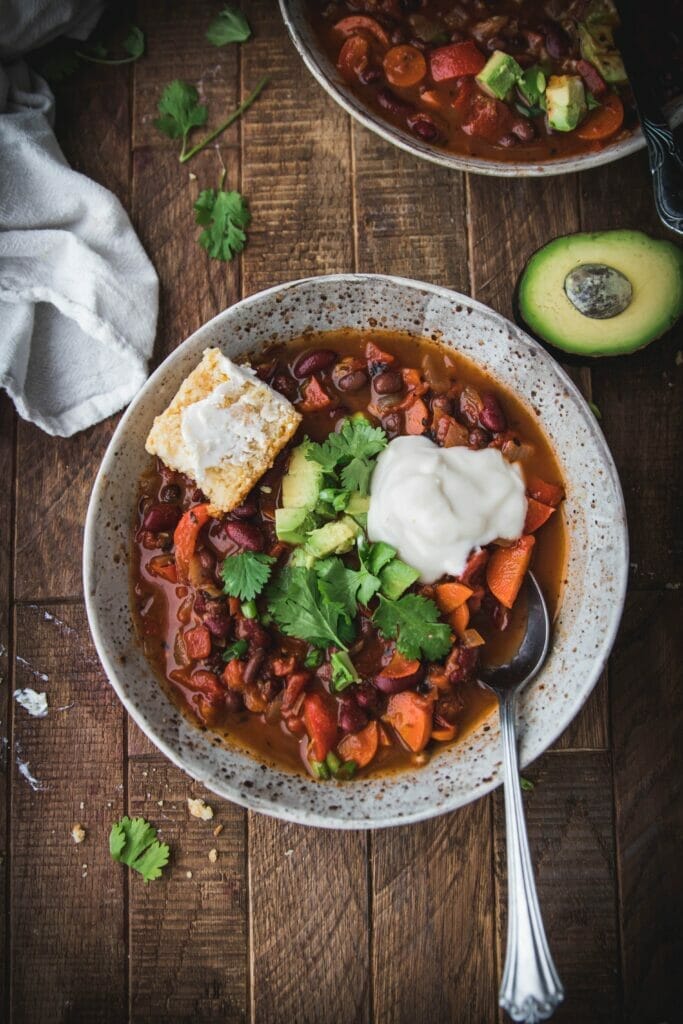 overhead shot of easy vegan chili topped with sour cream, avocado, and a slice of cornbread