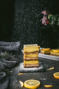stack of three meyer lemon cheesecake bars on a black table with a sprinkle of powdered sugar