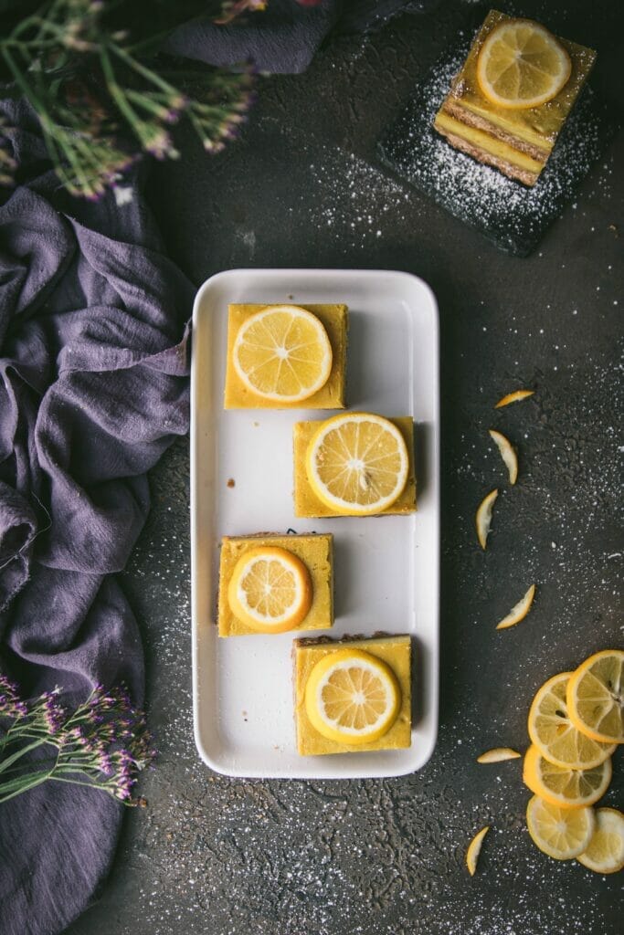 four vegan lemon cheesecake bars on a white tray shot from overhead