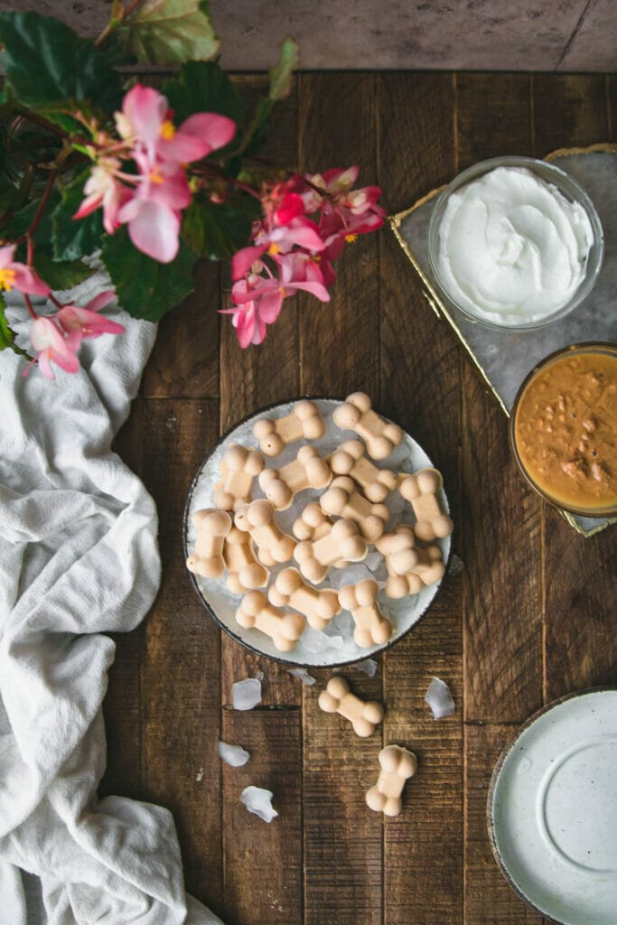 overhead shot of a bowl of frozen dog treats on a wooden table next to peanut butter