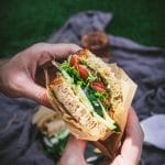 hands holding a vegan california veggie sandwich over a picnic