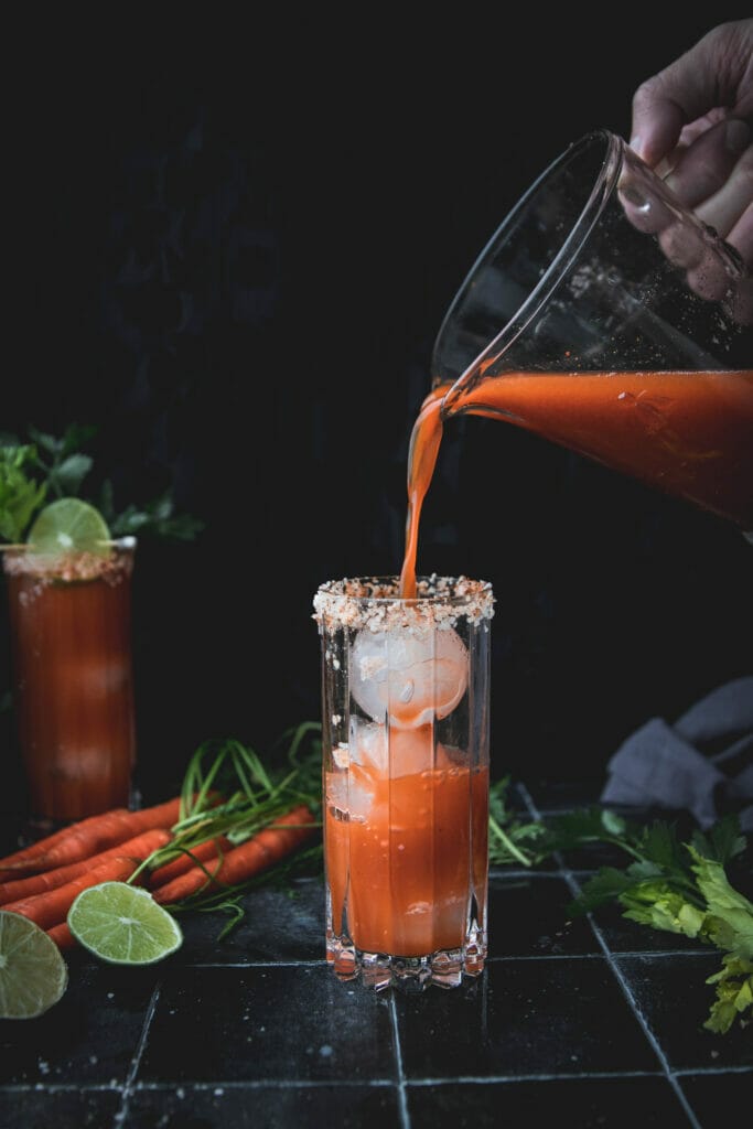 carrot bloody mary being poured into a tall glass