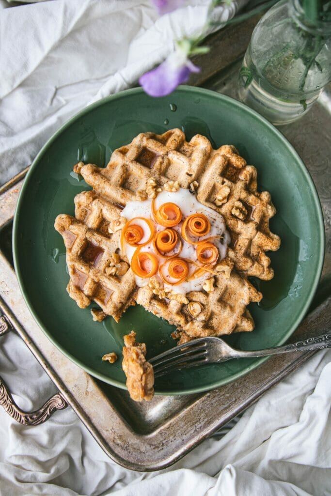 fork taking one piece of a vegan carrot cake waffle set on top of a bed on a silver tray