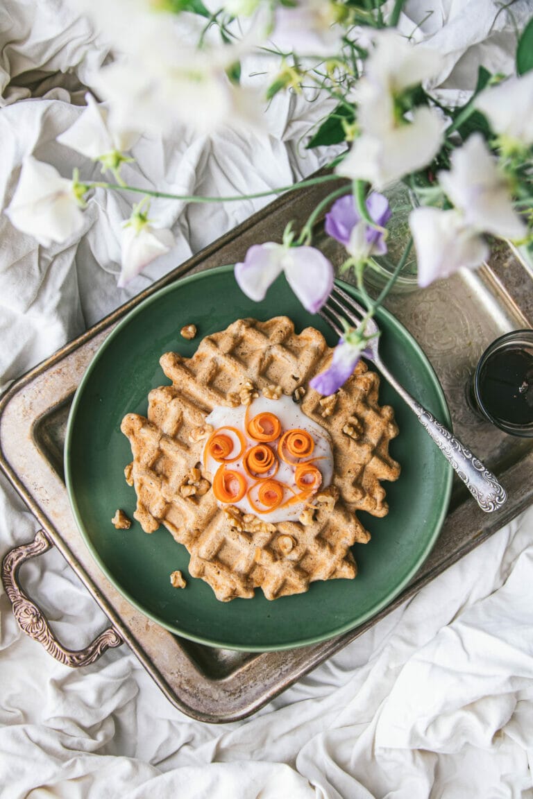 vegan carrot cake waffle on a breakfast tray next to a vase of flowers