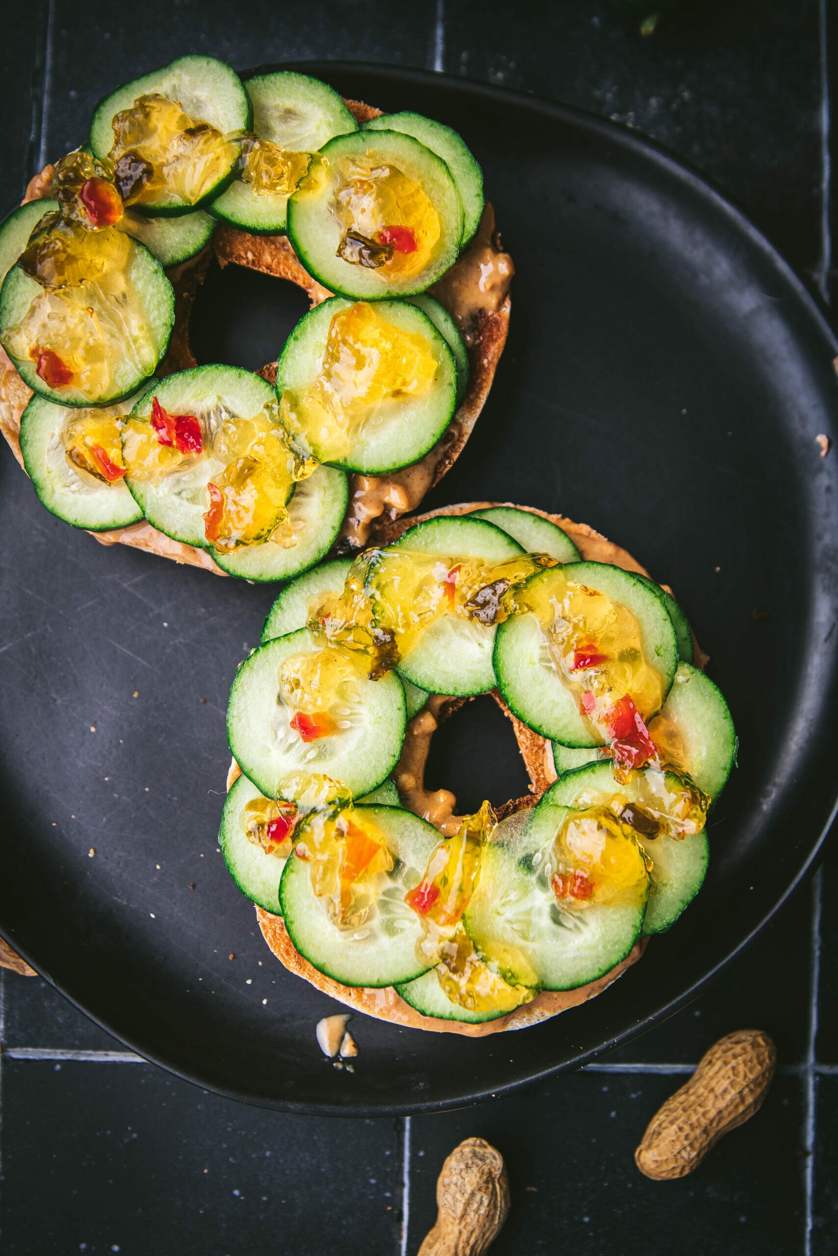 overhead shot of a sliced open thai peanut bagel with cucumber slices and jalapeño jam