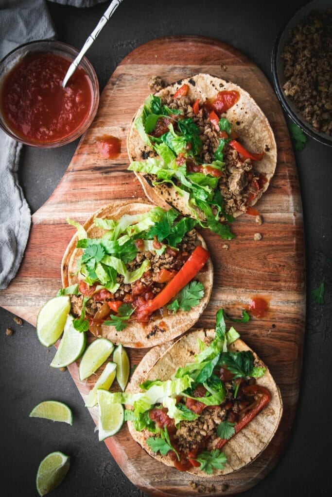 overhead shot of three walnut lentil tacos with peppers and onions on a circular wood board