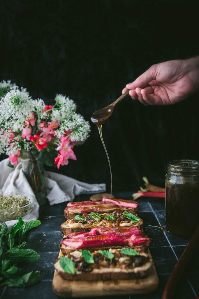 a hand drizzling honey over slices of roasted rhubarb sandwiches