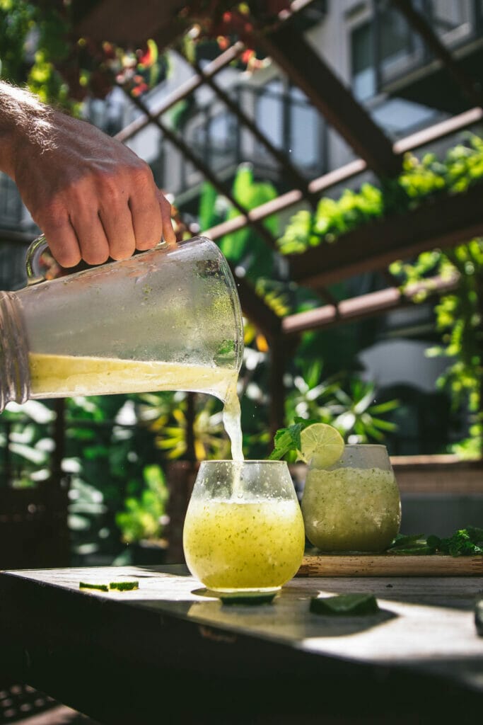 hand pouring a pitcher of frozen mojito slushies in a glass
