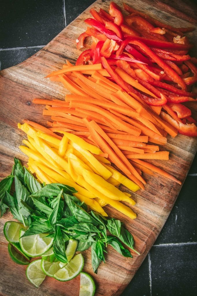 overhead shot of a rainbow of sliced red peppers, oranges, mango, basil, and lime