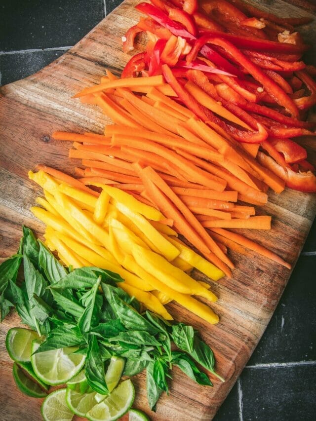 overhead shot of a rainbow of sliced red peppers, oranges, mango, basil, and lime