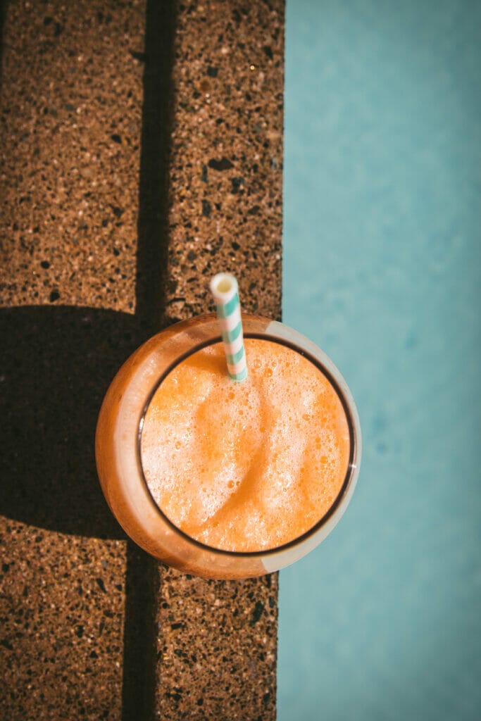 an overhead shot of a glass of melon agua fresca poolside with a straw