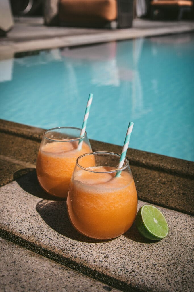 two glasses of melon agua fresca next to a pool