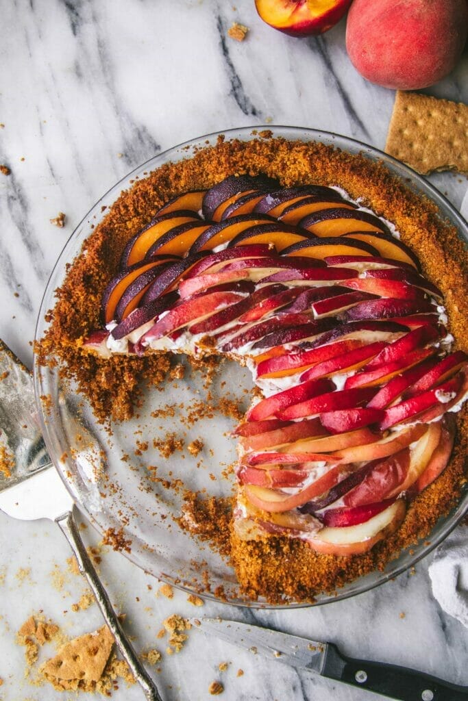 overhead shot of a sliced peaches and cream tart on a marble table