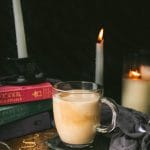 mug of vegan butterbeer on a wooden table next to candles and harry potter books