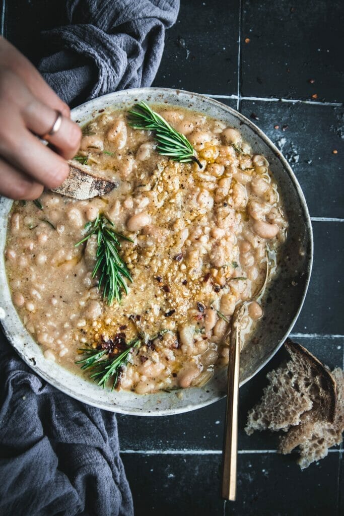 hand dipping bread into a pot of braised white beans