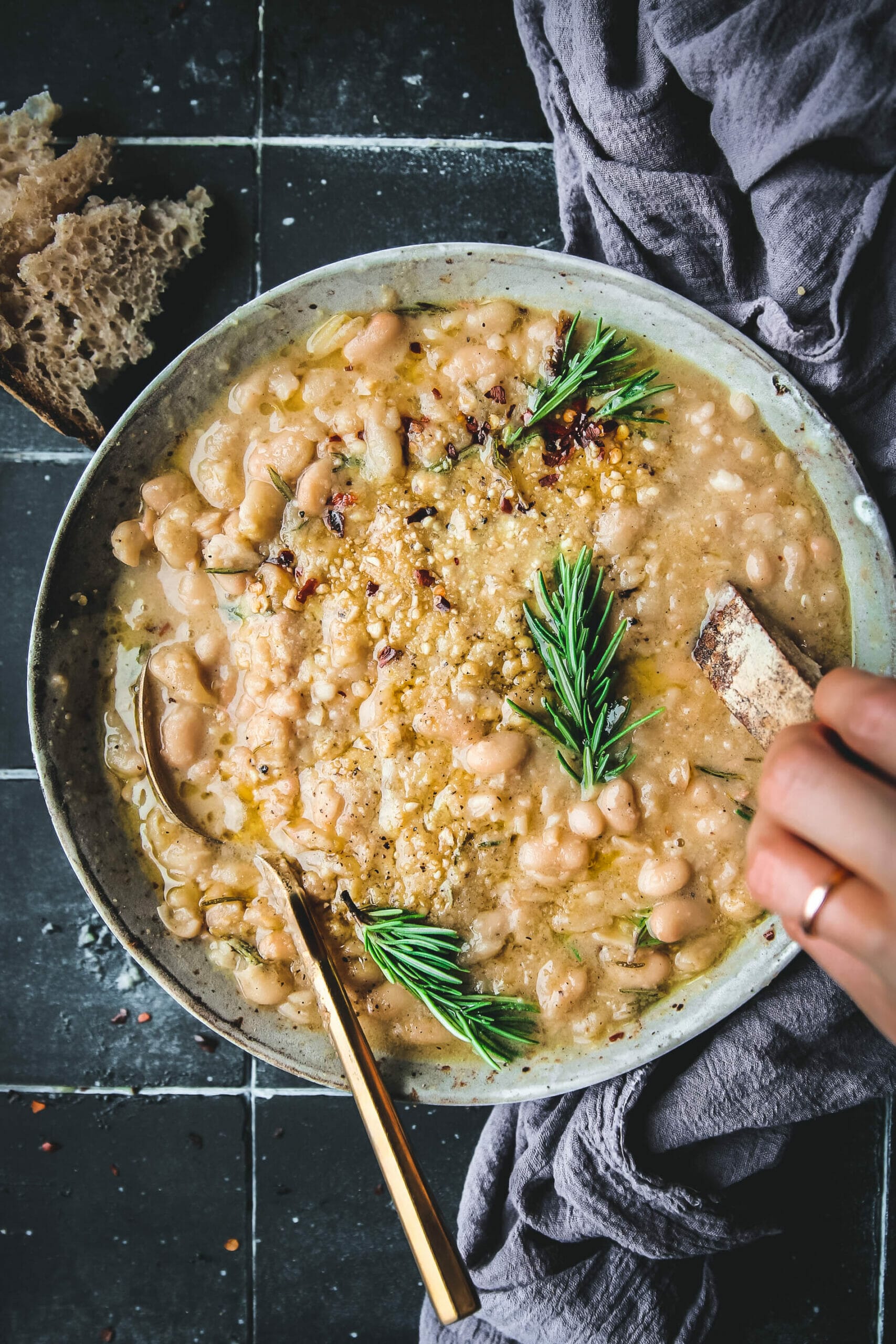 bowl of rosemary garlic braised white beans with a gold spoon and crusty bread