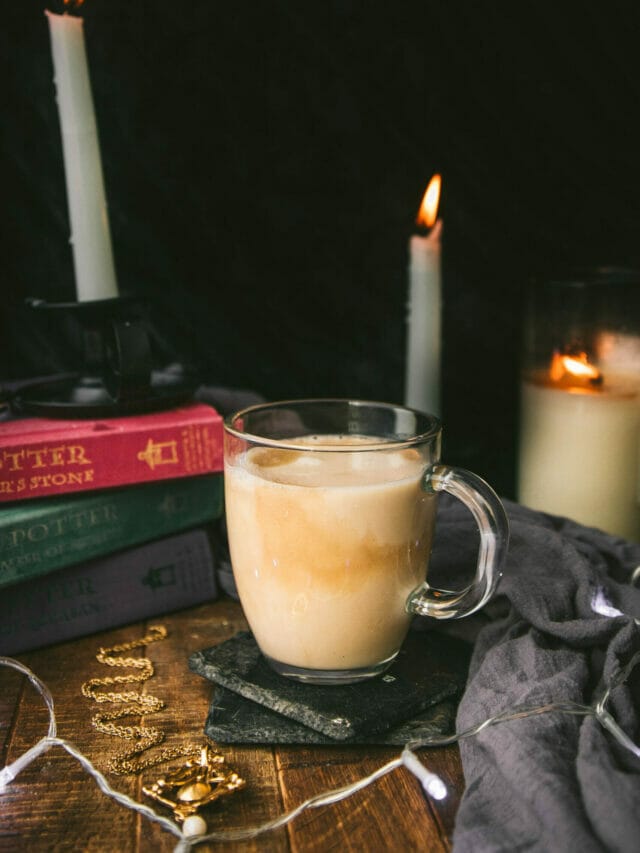mug of vegan butterbeer on a wooden table next to candles and harry potter books
