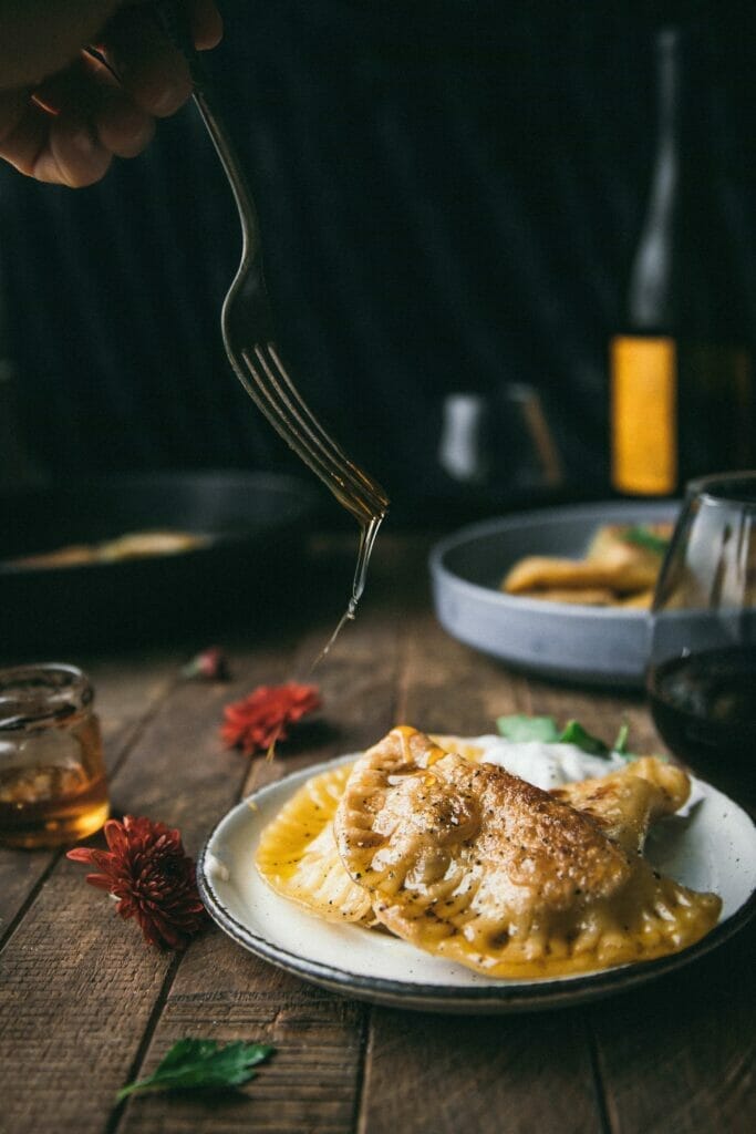 a fork drizzling honey on top of a plate of pumpkin pierogi