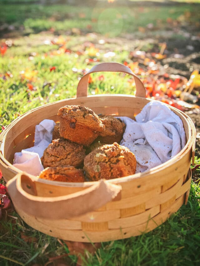 a side view of a basket of vegan pumpkin muffins next to fall leaves