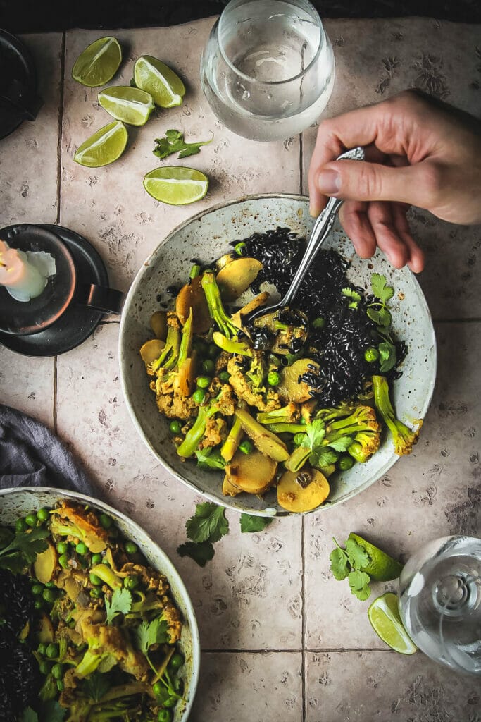 hand with spoon reaching into a bowl of turmeric cauliflower and peas