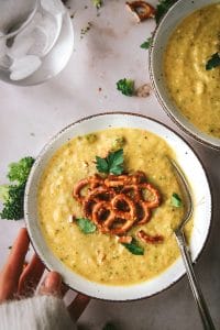 bowl of vegan broccoli cheddar soup topped with pretzels