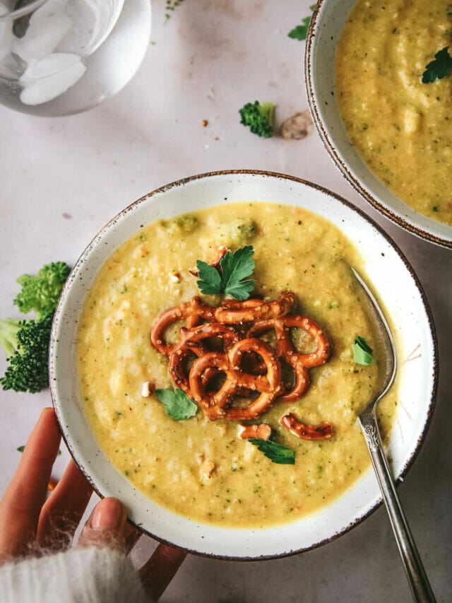 bowl of vegan broccoli cheddar soup topped with pretzels