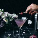 hand placing a cherry on top of a lavender haze cocktail