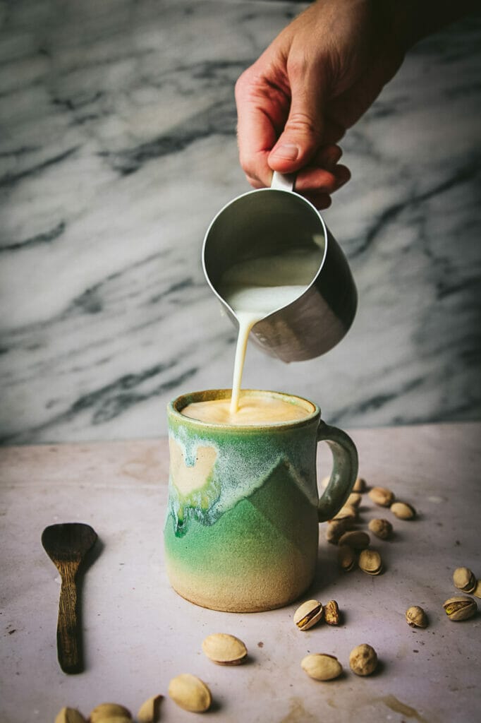 hand pouring frothed oat milk into a mug